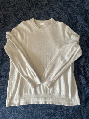 Beige stickad tröja från Filippa K - En stilren beige stickad tröja från Filippa K med rund halsringning och långa ärmar. Tröjan har en klassisk passform och är tillverkad i ett mjukt material som passar perfekt för lager-på-lager. Enkel och tidlös design.
