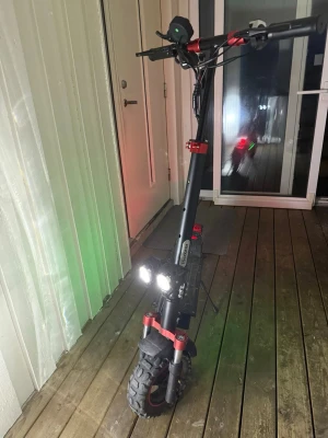 Svart och röd elscooter med stora hjul - Elscooter i svart med röda detaljer och grova terrängdäck. Utrustad med dubbla starka LED-strålkastare framtill och robust ram. Styrstången har flera förstärkningar och display. Perfekt för dig som vill ha en kraftfull och cool elsparkcykel. 45 kmh