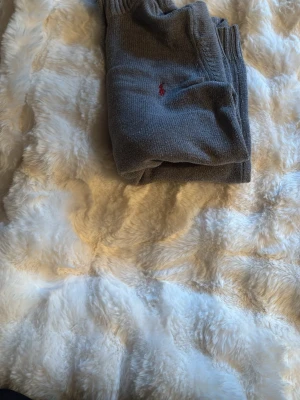 Grå tröja från Polo Ralph Lauren - Säljer en stilren grå tröja från Polo Ralph Lauren med halv dragkedja och ribbade muddar. Tröjan har en liten röd logga broderad på bröstet och är tillverkad i mjukt stickat material. Perfekt för dig som gillar klassisk och enkel stil.