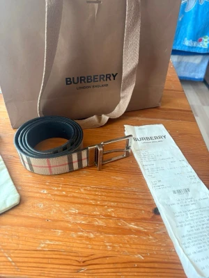 Burberry rutigt bälte i skinn - Snyggt bälte från Burberry med klassiskt rutig design i beige, rött och svart. Bältet har silverfärgat spänne och är gjort i skinn med tygdetaljer. Perfekt accessoar för att lyfta din outfit. Bältet går vända ut och in om man vill köra på svart färg lite repor men man tänker inte på det direkt