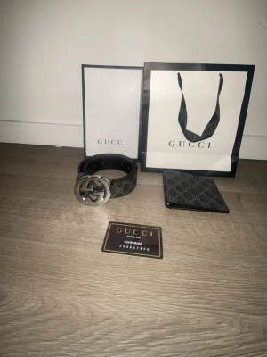 Svart Gucci bälte med GG-spänne - Snyggt svart bälte från Gucci med klassiskt GG-mönster och stort silverfärgat GG-spänne. Bältet är gjort i skinn och har exklusiv känsla. Perfekt accessoar för att lyfta din outfit med en lyxig touch.