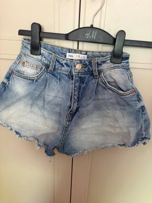 Blå baggy jeans från Gina - Säljer ett par blå dfrån Zara med fransig nederkant och klassisk femficksdesign. Shortsen har en hög midja och är tillverkade i bomull. Perfekta för sommarens alla äventyr, snygga att matcha med en enkel t-shirt eller hoodie.
