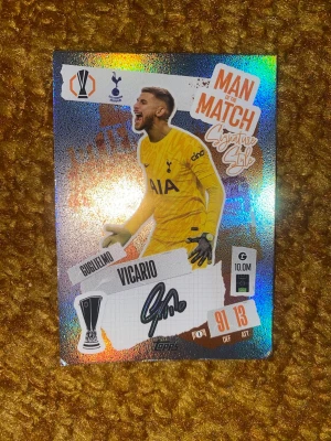 Fotbolls kort  - Säljer ett glittrigt Match Attax samlarkort med Guglielmo Vicario från Tottenham Hotspur. Kortet har texten 'Man of the Match Signature Style' och visar Vicario i gul målvaktströja. Perfekt för dig som samlar på fotbollskort eller gillar Tottenham.