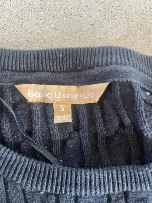 Svart kabelstickad tröja Basic U - Kabelstickad svart tröja från Basic U collection i storlek S. Tröjan har rund halsringning, långa ärmar och ribbade muddar vid ärmslut och nederkant. Perfekt för lager på lager och enkel att matcha med olika outfits.