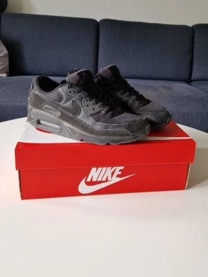 Nike Air Max 90 svarta sneakers - Grymt snygga svarta Nike Air Max 90 sneakers med klassisk design och ikonisk sula. Skorna har mesh och läderdetaljer, samt en synlig Air-enhet i hälen. Perfekta för dig som vill ha en stilren och tidlös look. Använda med lite slitage vid hälen, inte som märks vid användning. 