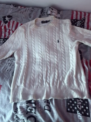 Vit kabelstickad tröja Polo Ralph Lauren - Kabelstickad vit tröja från Polo Ralph Lauren med rund halsringning och diskret broderad logga på bröstet. Tröjan har långa ärmar och ribbade muddar vid ärmslut och nederkant. Klassisk och stilren design i mjukt material. Funkar för S också. PRIS KAN DISKUTERAS.
