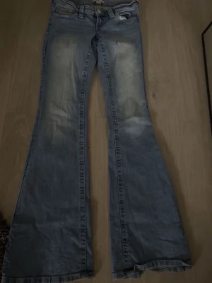 Blå utsvängda jeans bootcut - Säljer ett par blå bootcut jeans med utsvängda ben och klassisk femficksmodell. Jeansen har ljusa slitningar framtill och är tillverkade i denim. Perfekta för dig som gillar retrostil och vill ha ett par jeans med riktigt snygg passform.