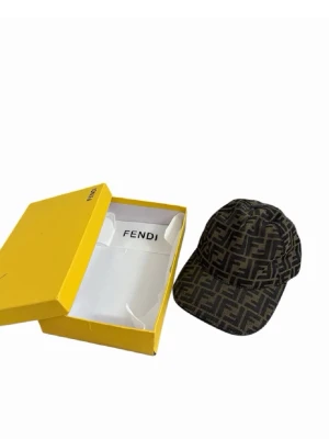 Fendi keps med FF-mönster - Snygg keps från Fendi i brunt och svart med det klassiska FF-logomönstret över hela kepsen. Kepsen har böjd skärm och justerbar baksida. Tillverkad i ett slitstarkt tygmaterial som ger en exklusiv känsla. Perfekt för dig som vill sticka ut med en lyxig accessoar.