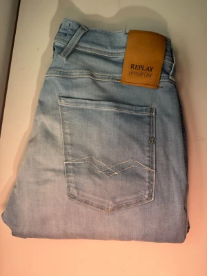 Ljusblå Replay Hyperflex jeans - Säljer ett par ljusblå Replay Hyperflex jeans, modell Anbass. Jeansen har klassisk femficksdesign, snygga sömdetaljer på bakfickan och en läderpatch med logga i midjan. Tillverkade i stretchigt denim för extra komfort. LENGHT 32 WAIST 31 byxorna är lite avklippta vid benen