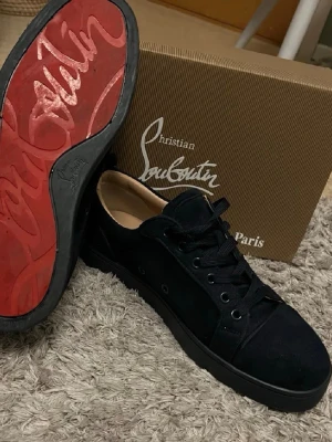 Svarta sneakers från Christian Louboutin - Stilrena svarta sneakers från Christian Louboutin i mocka med klassisk röd sula och svarta skosnören. Låg modell med diskreta detaljer och exklusiv känsla. Perfekta för dig som vill ha något unikt och trendigt i garderoben.