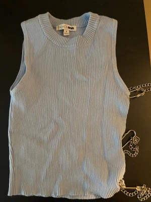 Ljusblå ribbad linnetopp Fashion Nova - Trendig ljusblå ribbad linnetopp från Fashion Nova. Toppen är ärmlös och har unika kedjedetaljer med fjärilar och säkerhetsnålar på sidan.