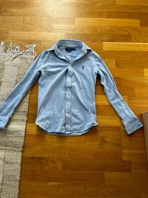 Ljusblå skjorta från Ralph Lauren - Klassisk ljusblå skjorta från Ralph Lauren med broderad logga på bröstet. Skjortan har långa armar. Perfekt för en clean och stilren look.