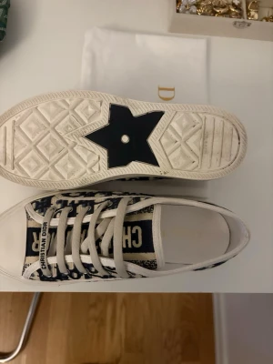 Dior låga sneakers Walk’n’dior 38 - Walk’n’dior/ Snygga låga sneakers från Dior med klassiskt blått och vitt Oblique-mönster. Skorna har vita snören, gummisula med stjärndetalj och tydlig Christian Dior-logga på plösen. Tillverkade i canvas och gummi för en trendig och exklusiv look.
