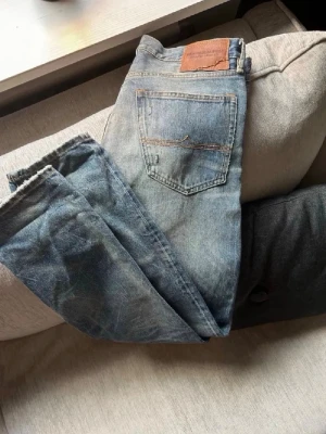 Ljusblå vintage Ralph lauren jeans - Säljer ett par ljusblå Ralph lauren jeans med slitningar och patchdetaljer på benen. Jeansen har klassisk femficksmodell, rak passform och läderpatch bak i midjan. Perfekta för en avslappnad och trendig look.