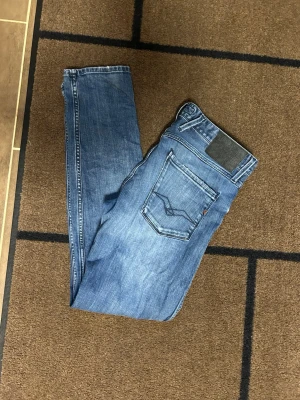 Blå slim fit jeans från Replay - Snygga blå slim fit jeans från Replay med klassisk femficksdesign och lätt slitna detaljer. Jeansen har normal midja, smala ben och är tillverkade i denim med stretch för extra komfort. Perfekta för en trendig och avslappnad look. 32/32