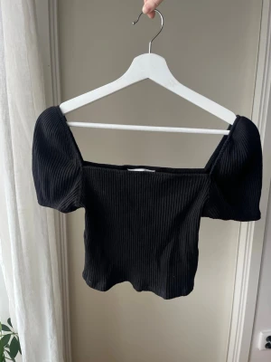 Svart ribbad croppad topp - Trendig svart croppad topp med puffiga korta ärmar och ribbad struktur. Sitter snyggt både offshoulder/eller på axlarna. 