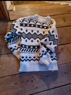 Beige och svart stickad tröja - Stickad tröja i beige med svart nordiskt mönster. Tröjan har rund halsringning, ribbade muddar och nederkant. Perfekt för kalla dagar och ger en mysig vibe. Mönstret består av zigzag och geometriska former.