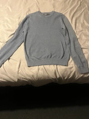 Ljusblå stickad tröja Dressmann - Snygg ljusblå stickad tröja från Dressmann med rund halsringning och ribbade muddar vid ärmslut och nederkant. Enkel och stilren design som passar perfekt till jeans eller chinos. Tillverkad i mjukt material för skön känsla. Pris kan diskuteras 