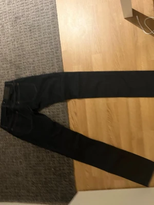 Svarta raka jeans i klassisk modell - Säljer ett par svarta jeans från tiger of sweden med rak passform och klassisk femficksdesign. Jeansen har normal midja och är tillverkade i ett mörkt denimtyg som ger en stilren look. Perfekta för dig som gillar en enkel och tidlös stil. Storlek W 26 L 32, hör av er vid funderingar!