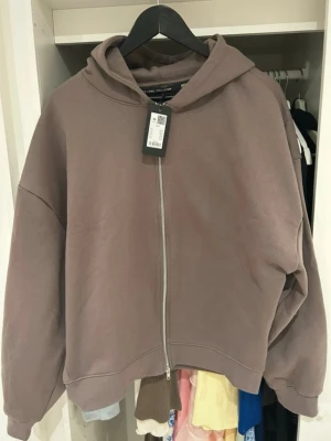 Brun zip hoodie - Snygg brun hoodie med dragkedja framtill och luva. Oversized passform. Aldrig använd men min sambo drog av lappen för fort innan han insåg att den inte passa. 
