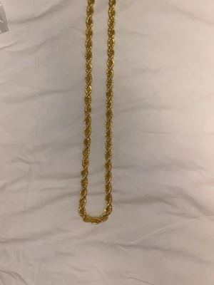 Flätat guldfärgat halsband - Snyggt halsband i guldfärg med flätad design som ger en chunky och trendig look. Halsbandet har en glansig finish och passar perfekt för att lyfta vilken outfit som helst. Materialet ser ut att vara metall med en guldfärgad yta.