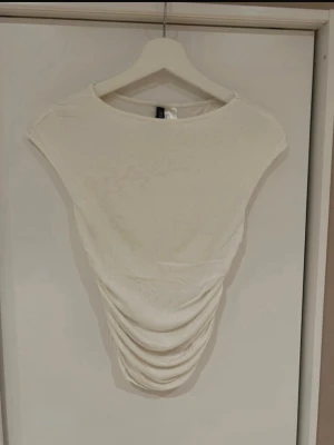 Vit topp - Säljer en vit ärmlös topp från H&M med rynkade detaljer framtill och baktill.