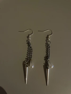 Livia earrings  - Säljer ett par coola silvriga örhängen med kedjor, spetsiga konformade hängen och droppformade vita pärlor. Örhängena har en edgy stil och är perfekta för att ge din look lite extra attityd.💗