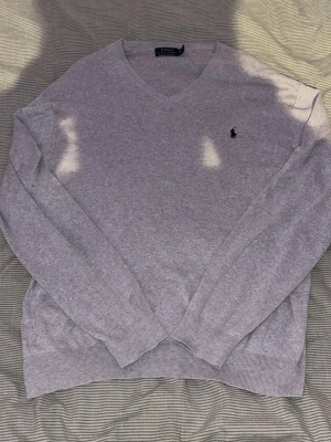 Grå v-ringad tröja från Polo Ralph Lauren - Klassisk grå v-ringad tröja från Polo Ralph Lauren med den ikoniska broderade loggan på bröstet. Tröjan har långa ärmar, ribbade muddar.