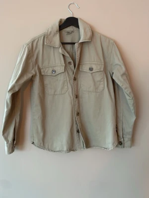 Grön overshirt med fickor - Stilren grön overshirt med två bröstfickor och knappar framtill. Skjortkrage och långa ärmar ger en avslappnad look. Tillverkad i ett mjukt bomullstyg som känns bekvämt mot huden. Perfekt att bära öppen över en t-shirt.