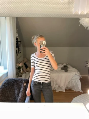 Randig ribbad topp med rund hals - Säljer en vit ribbad topp med svarta horisontella ränder och rund halsringning. Toppen har korta ärmar och en slim passform som sitter snyggt på kroppen. Perfekt att styla med jeans eller kjol för en enkel och fräsch look.