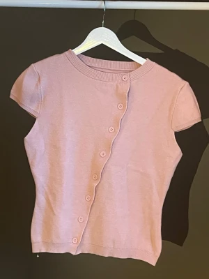 Ljusrosa kortärmad kofta - Supersöt ljusrosa kofta med korta ärmar och sned knäppning framtill. Koftan har rund halsringning och ribbade kanter. Perfekt för att addera en mjuk touch till din outfit. Materialet känns mjukt och lättstickat. Köpt på Sellpy, aldrig använd🌸