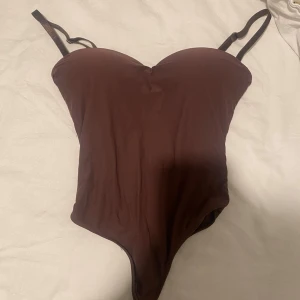 Body brun H&M - Snygg brun body med tunna, justerbara axelband och vadderade kupor. Mjuk och stretchig känsla, köpt från h&m som nu är slutsåld. Bodyn har aldrig använts och priset kan diskuteras!