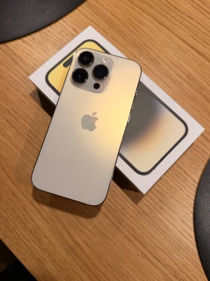 iPhone 14 pro - Snygg iPhone 14 pro i guld med originalkartong. I mycket bra skick då jag alltid haft skärmskydd och mobilskal samt varit väldigt rädd om den. Det är 128gb och har några små repor vilket syns på bilderna. Kvitto finns självklart och telefonen är i mycket gott skick och har okej batterikapacitet. Säljes då jag köpt iPhone 17. Medföljer 2 mobilskal och 2 skärmskydd, samt orörd originalmaterial med laddare. 