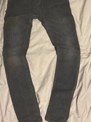 Grå slim fit jeans - Säljer ett par grå slim fit jeans med klassisk femficksdesign och dragkedjegylf. Jeansen har en snygg tvättad look och smal passform som sitter tajt längs benen. Perfekta för en stilren och modern outfit.kommer inte med prislappen 