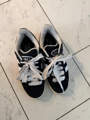 Svarta Adidas sneakers med vita ränder - Klassiska svarta Adidas sneakers med vita ränder och vit sula. Använda ett fåtal gånger och är i bra skick! Lite defekter i självaste skon utöver det är det som nya 