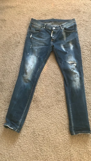 Dsquared2 - Säljer ett par blå DSQ2 slim jeans med slitningar och hål på benen för en trendig, avslappnad look. Jeansen har fem fickor, dragkedjegylf och är tillverkade i denim. Kan ändra priset