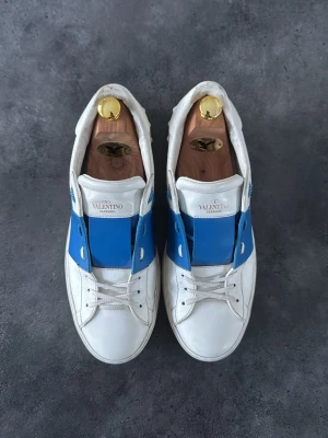 Blåa Valentino Open  - Säljer ett par vita Valentino Opens med blått sträck. Skorna är inte nyskick men mycket bra skick, allt i bilderna ingår, pris kan diskuteras vid snabb affär ✅