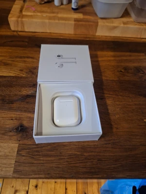 Apple AirPods med laddningsetui - Säljer ett par vita Apple AirPods med tillhörande laddningsetui. Snygg och kompakt design i blank plast, perfekt för dig som vill ha trådlösa hörlurar med smidig laddning. Passar till både iPhone och andra enheter med Bluetooth.