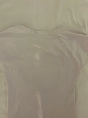 Ljusrosa tight topp med djup urringning - Säljer en vitt topp med tight passform och öppen rygg. Toppen är kortärmad och tillverkad i ett stretchigt syntetmaterial som sitter snyggt på kroppen. Perfekt att styla med jeans eller kjol för en trendig look. ❤️😘