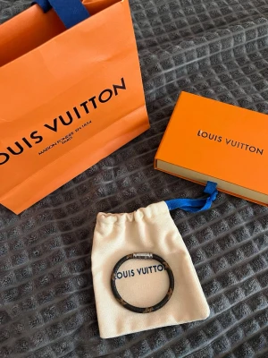 Louis Vuitton armband - Armband från Louis Vuitton (orginalpris 225€). Brunt läder (osäker om det är riktigt eller faux) med silver magnetspänne. Kommer med originalpåse och ask. Armbandet var en gåva och därför har jag tyvärr inget kvitto. Ca 17,5 cm och 5,5 cm i diameter. 