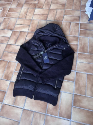 Leon Marcel Hybridjacka – Midnight Navy | Ny Med Prislapp - Ny med prislapp — Leon Marcels hybridjacka i djup midnattsblå med quiltad pufferkropp och stickade ärmar. Avtagbar huva och lyxiga microfleecefickor som håller händerna varma. Tidlös Skandinavisk design som passar till allt. Perfekt för höst/vinter — och ett snyggt val även under kyliga vårdagar. Säljer direkt för att erbjuda ett bättre pris än butik. 📦 Spårad frakt, väl förpackad.