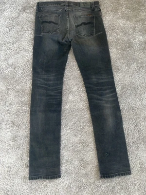  Nudie Jeans Lean Dean - Säljer ett par svarta jeans från Nudie Jeans med snyggt slitna detaljer och raka ben. Jeansen har klassiska bakfickor med Nudie Jeans signaturbrodyr och är tillverkade i mjuk denim. Perfekta för en avslappnad och trendig look. 30/32