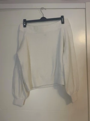 Offshoulder tröja - Säljer en enkel och snygg vit stickad tröja i storlek M. Tröjan har bred ribbad mudd i nederkant och vid ärmslut samt ballongärmar som ger en trendig look. Perfekt att matcha med jeans eller kjol för en clean stil.