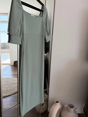 Ljusgrön långklänning med puffärm - Trendig ljusgrön långklänning med puffärmar och fyrkantig ringning. Klänningen har en rak passform och är tillverkad i ett ribbat material som ger en snygg struktur. Perfekt för dig som vill ha en stilren och modern look.