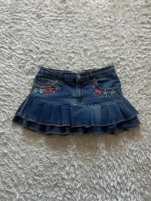 Blå volangkjol i denim med broderi - En Lågmidjad jeanskjol omsydd från ett par Levis jeans med volang och broderade blommor. 🌸   Midjemått tvärsöver - 35cm, stretchig. Längd - 30cm