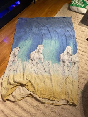 Påslakan med hästar och norrsken - Säljer ett påslakan med motiv av vita hästar som springer över en gul äng med blå och gröna norrskensfärger i bakgrunden. Materialet är bomull och motivet är tryckt över hela framsidan. Perfekt för dig som gillar hästar och färgstarka sängkläder.