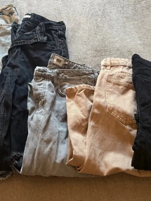 Mix av jeans i olika färger - Säljer ett gäng jeans i olika färger och tvättar – svart, ljusblå, beige och grå. Några har slitna detaljer och raka ben. Perfekta för dig som vill ha flera stilar att välja mellan. Märket 157 syns på ett par av jeansen. Klassisk femficksmodell.