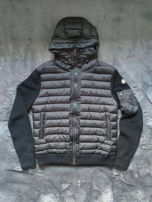 Moncler cardigan Nfc - Snygg svart pufferjacka från Moncler med stickade ärmar och quiltad kropp. Jackan har en vadderad huva, två dragkedjefickor fram och en extra ficka med dragkedja på ena ärmen. Perfekt för kalla vinterdagar och riktigt trendig look. Storlek M men passa oxå för S . Nfc funkar ✅
