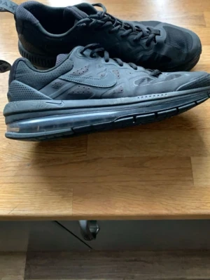 Svarta Nike Air Max sneakers - Säljer ett par helsvarta Nike Air Max sneakers med synlig luftdämpning i sulan. Skorna har en låg profil, mesh och syntetmaterial på ovandelen samt klassisk Nike-logga på sidan. Perfekta för dig som gillar sportig och clean stil.