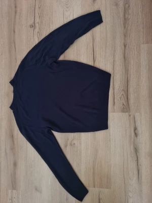 Mörkblå tröja från U.S. Polo Assn. - Mörkblå långärmad tröja från U.S. Polo Assn. med rund halsringning och diskret logga broderad på bröstet. Tröjan har ribbade muddar vid ärmslut och nederkant, vilket ger en klassisk och stilren look. Perfekt att matcha med jeans eller chinos.